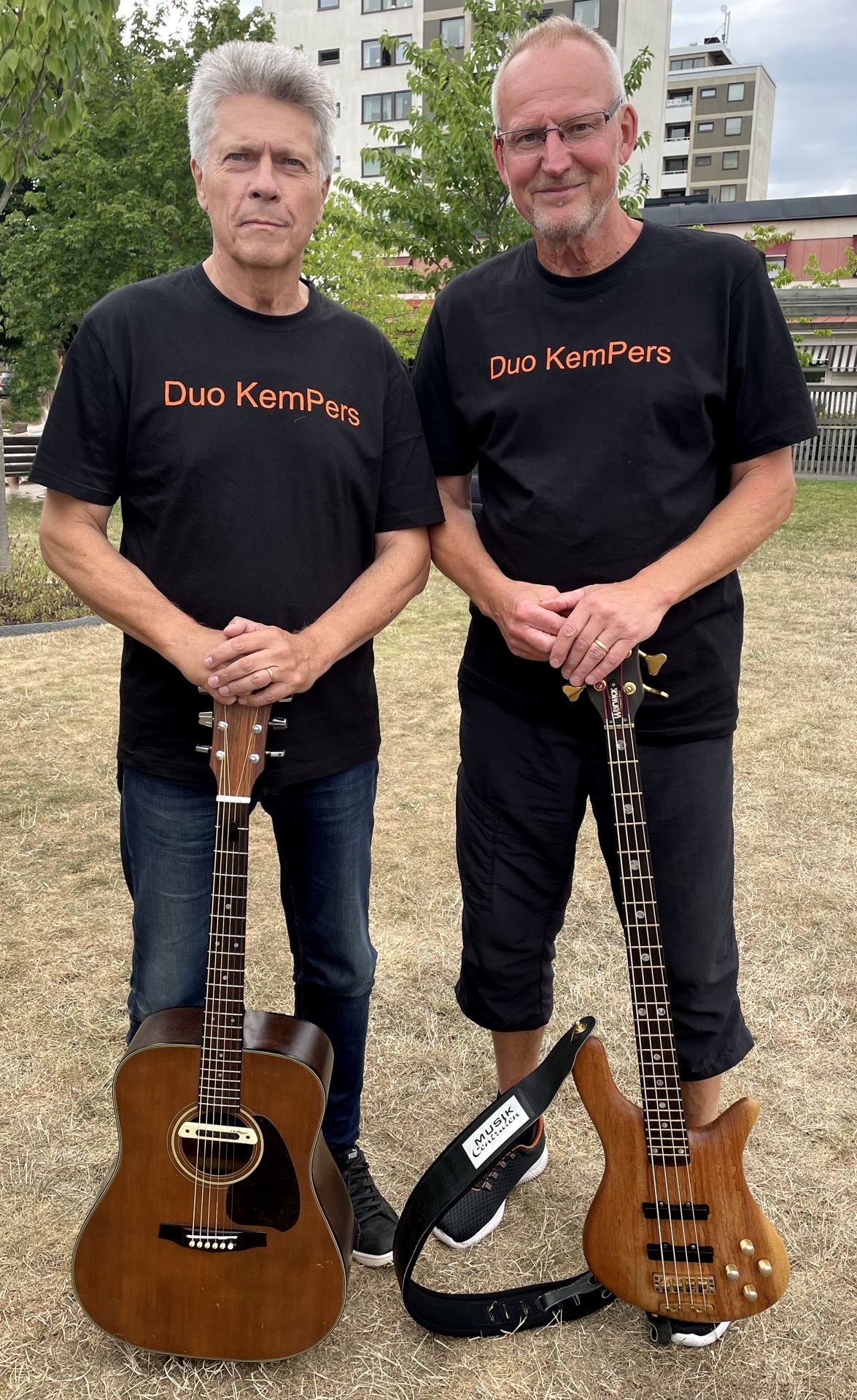 Benny Persner och Anders Kempe som utgör Duo KemPers står på en gräsmatta med varsin gitarr framför sig.