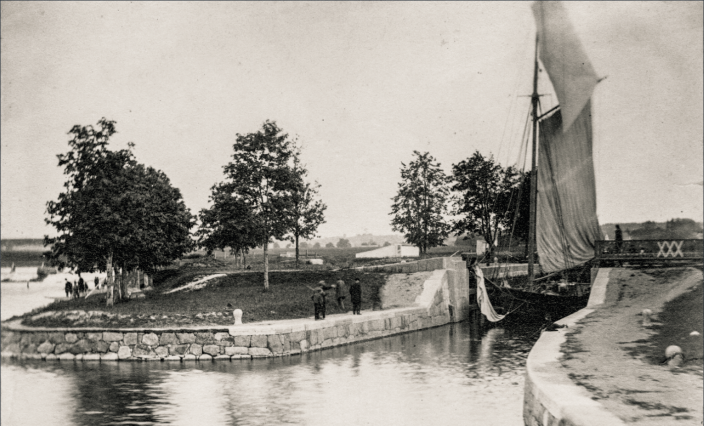 Svartvitt foto på en segelbåt på utgång nedanför en sluss.