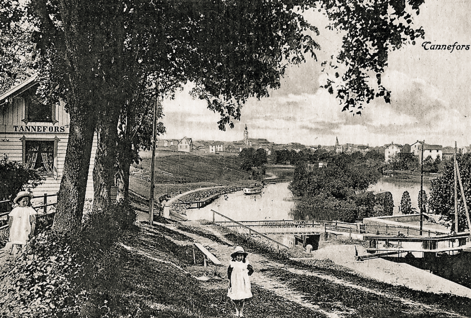 Svartvitt foto på en liten flicka som står framför Tannefors slussvaktarbostad. I bakgrunden syns Linköpings innerstad 